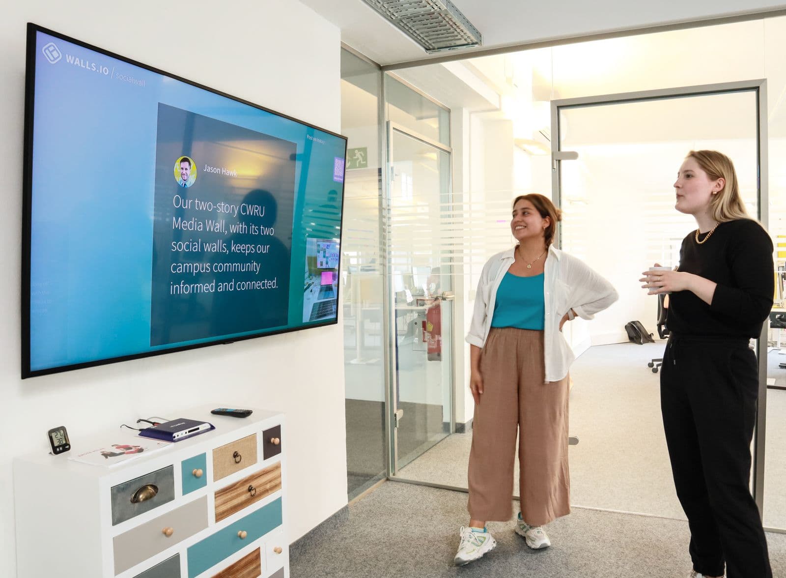 Two coworkers reviewing content on a large wall-mounted screen in a bright modern office